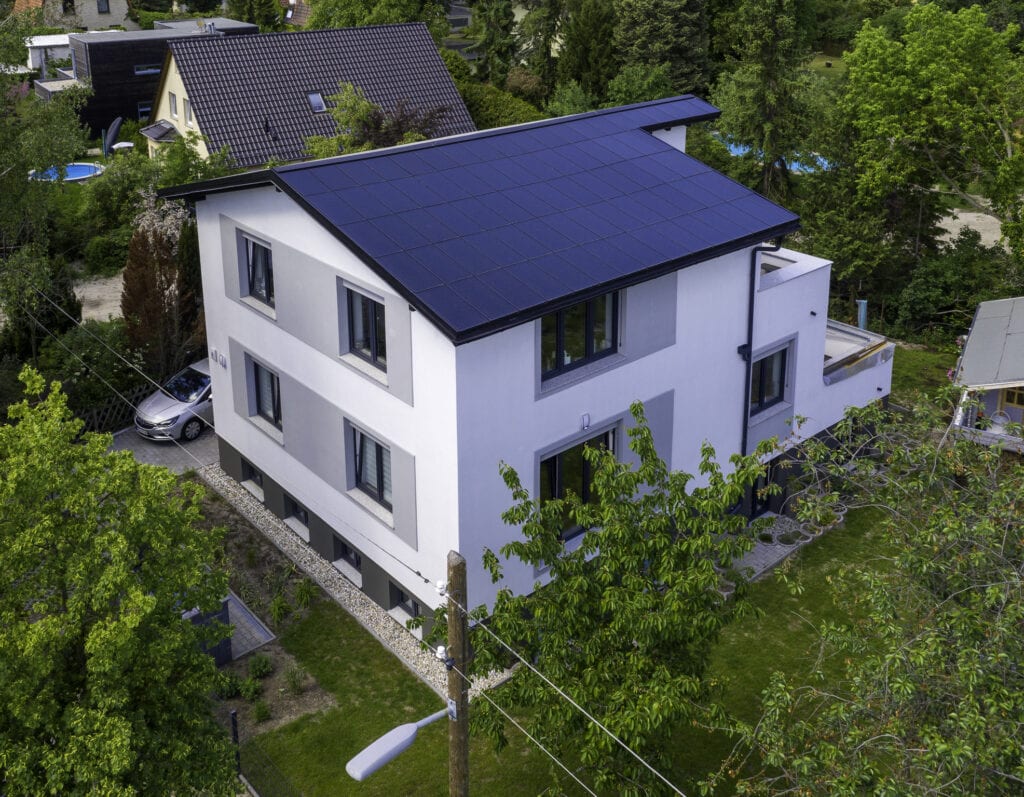 Ennogie-Solardach Berlin: Modernes Haus in weiß mit Ganzdachlösung für Photovoltaik, Bäume und Mast im Vordergrund