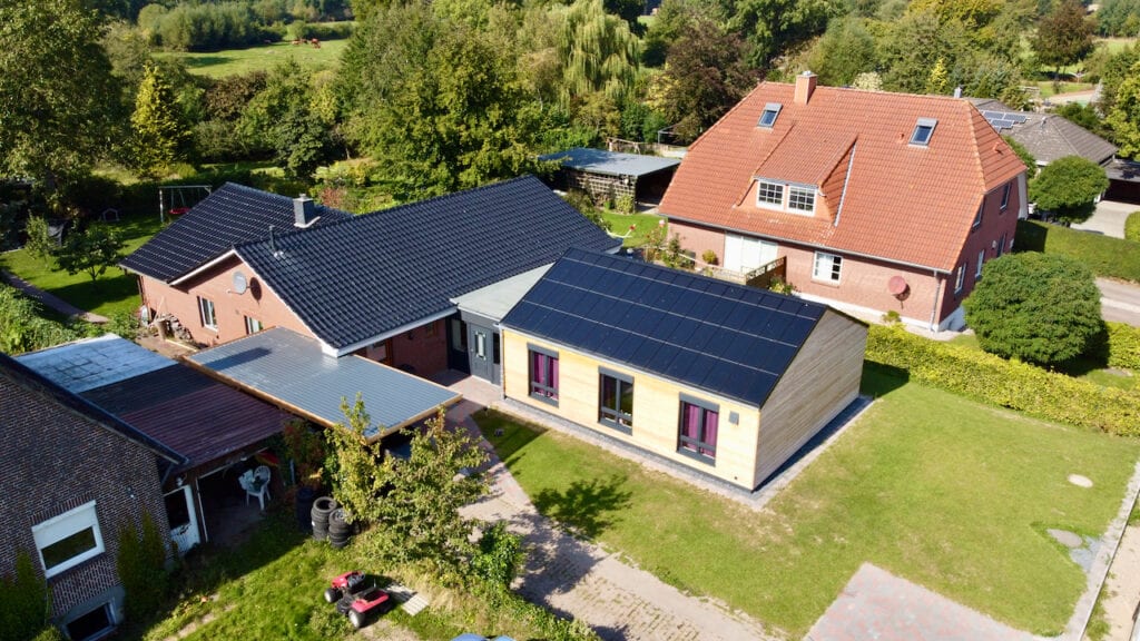 Ennogie-Solardach in Kalübbe: Totale mit einer Dachseite Photovoltaik und Abschlüssen sichtbar, Bäume und Nachbarschaft im Hintergrund