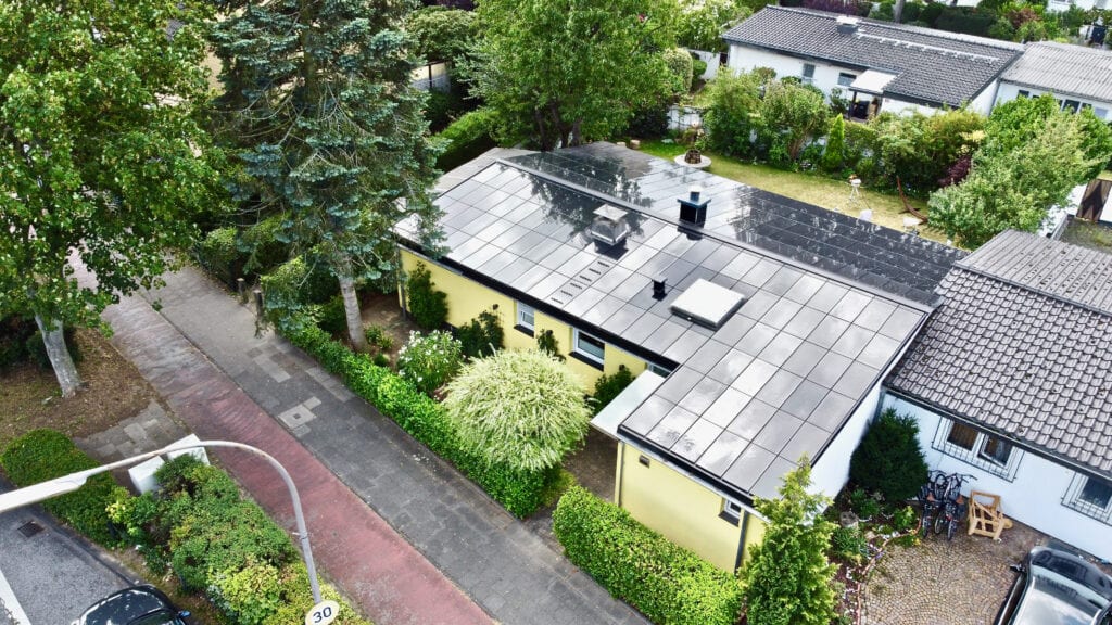 Ennogie-Solardach Bungalow in Köln: Vogelperspektive auf Dachfläche mit Ganzdachlösung für Photovoltaik belegt, umrahmt von Bäumen und Sträuchern