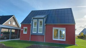 Nachhaltiges rotes Holzhaus mit Ennogie-Solardach von Architekt Lutze inklusive Carport und Garten